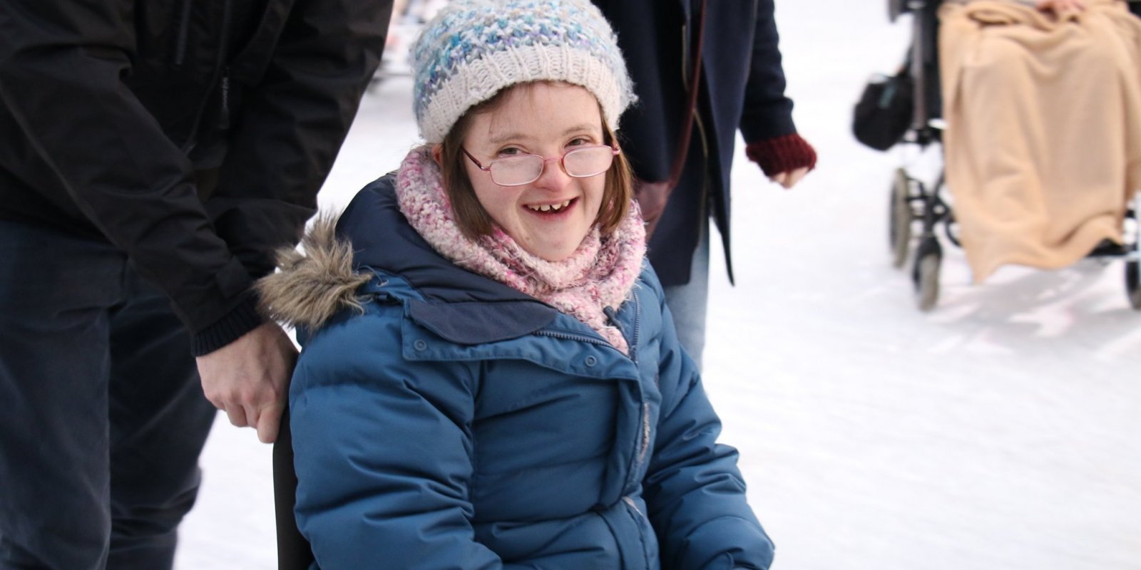 Cathers sat in wheelchair smiling with hat coat and glasses on on ice rink