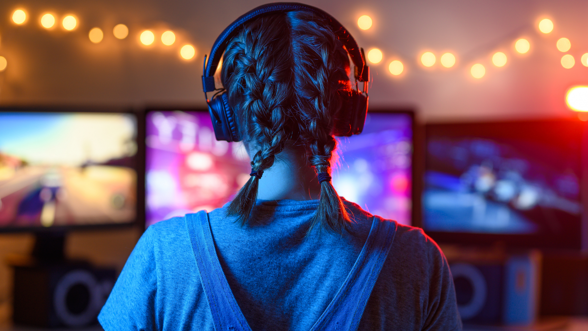 gamer girl with headphones is looking at pink glowing computer screens