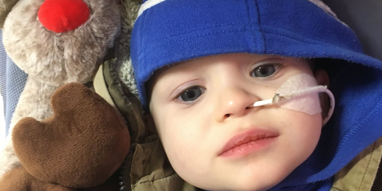 Baby boy with blue jumper with tube in nose cuddling reindeer