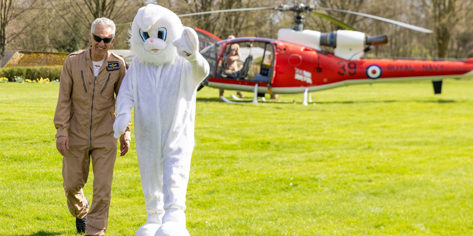 Easter bunny and pilot walking across green field with helicopter in background